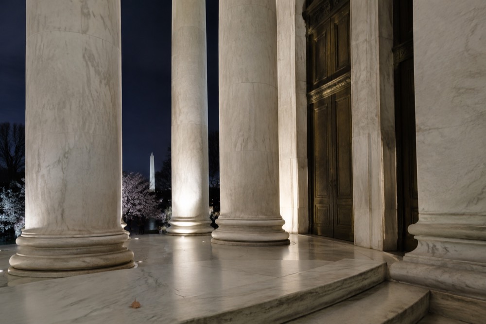 A lit marble memorial with columns glowing under uplights against a dark sky