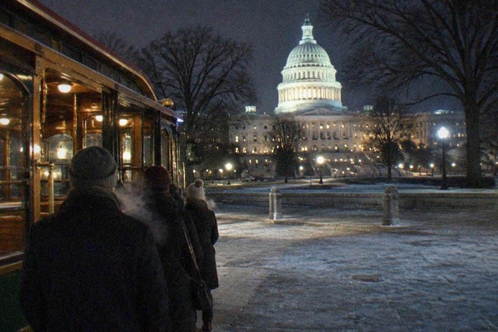 A vintage-style trolley lit from inside, waiting at a curb near the illuminated US Capitol