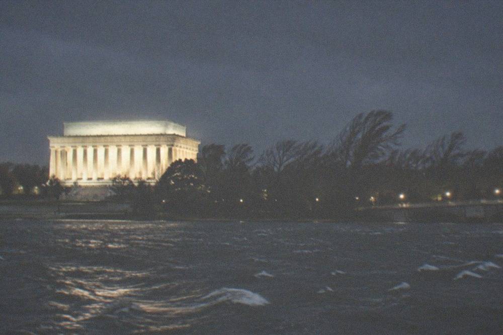 The Lincoln Memorial glowing white against a night sky, seen from a distance across dark water