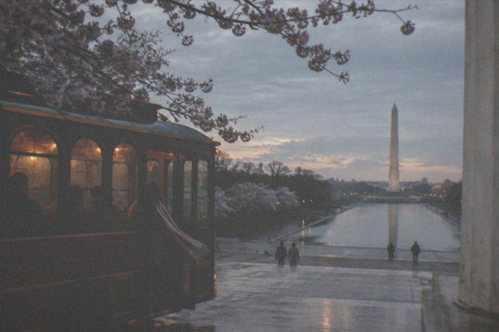 A vintage-style trolley parked near the Lincoln Memorial at dusk, its interior lights glowing as passengers board for a night tour