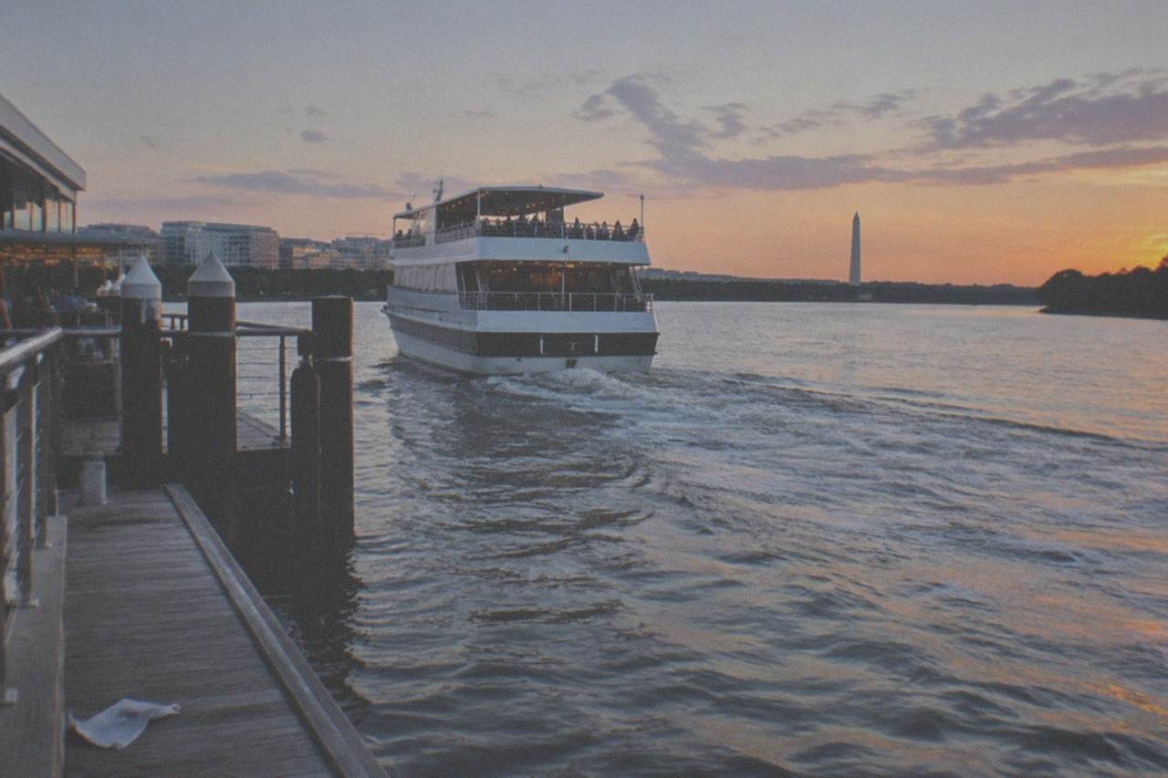 A dinner cruise boat on the Potomac River at dusk with the Washington Monument lit in the distance