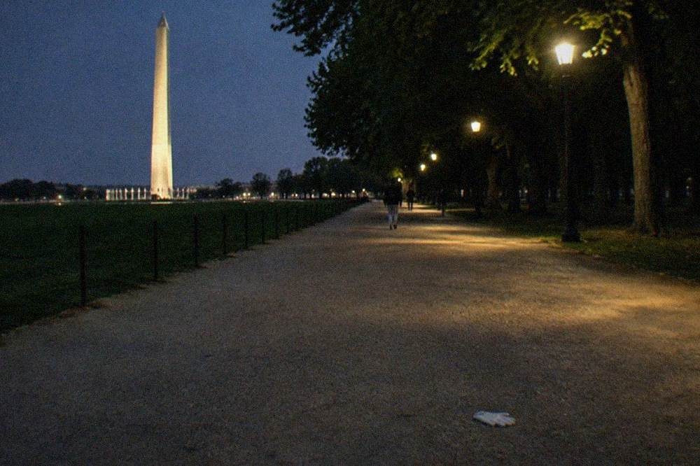 A wide empty walkway between lit memorials and trees at night