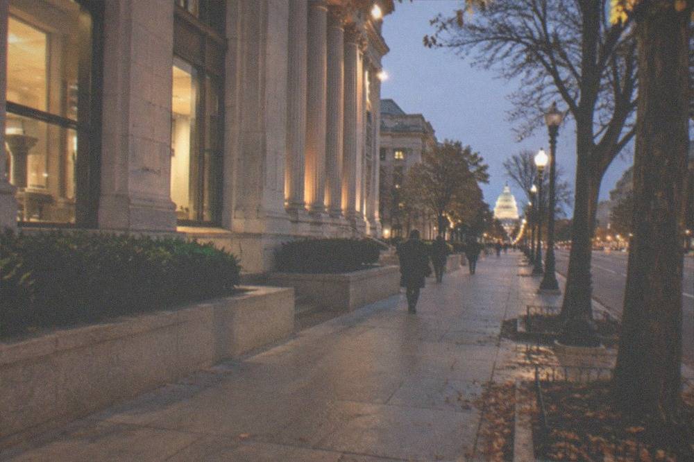 A city street with lit storefronts and a glowing dome visible in the distance