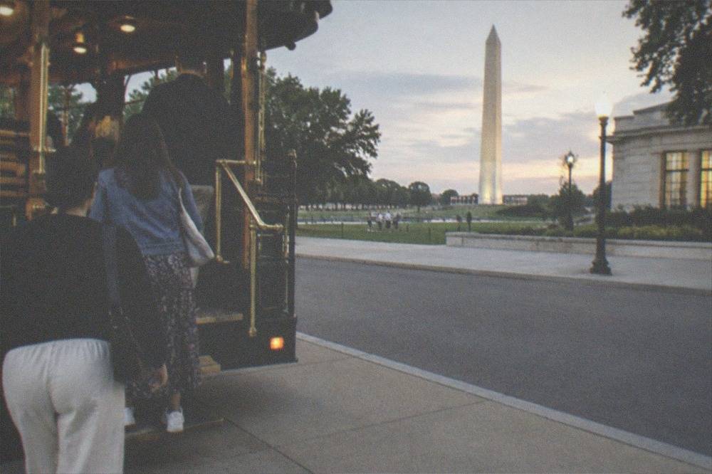 A group of visitors boarding a night tour trolley near the illuminated Washington Monument