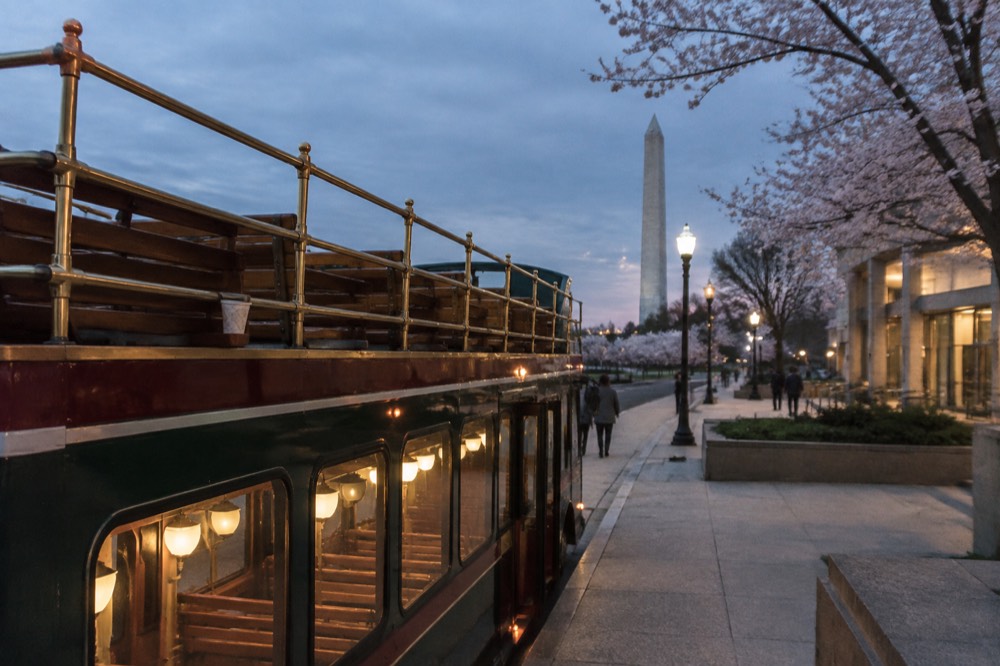 Open-top tour trolley parked beside illuminated memorial columns at night