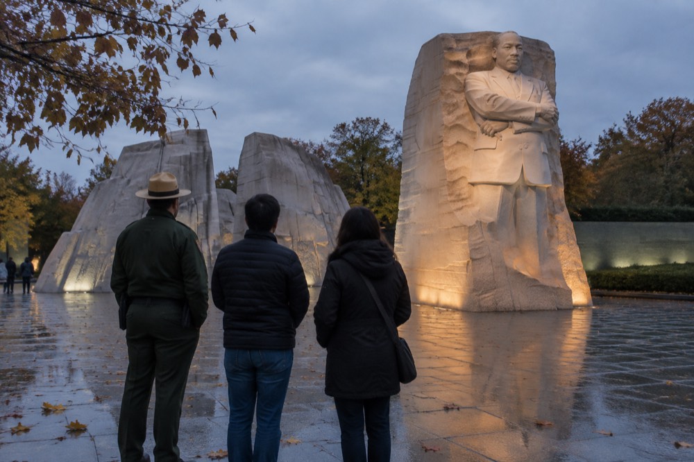 Park ranger speaking with visitors beside a lit memorial plaza at dusk