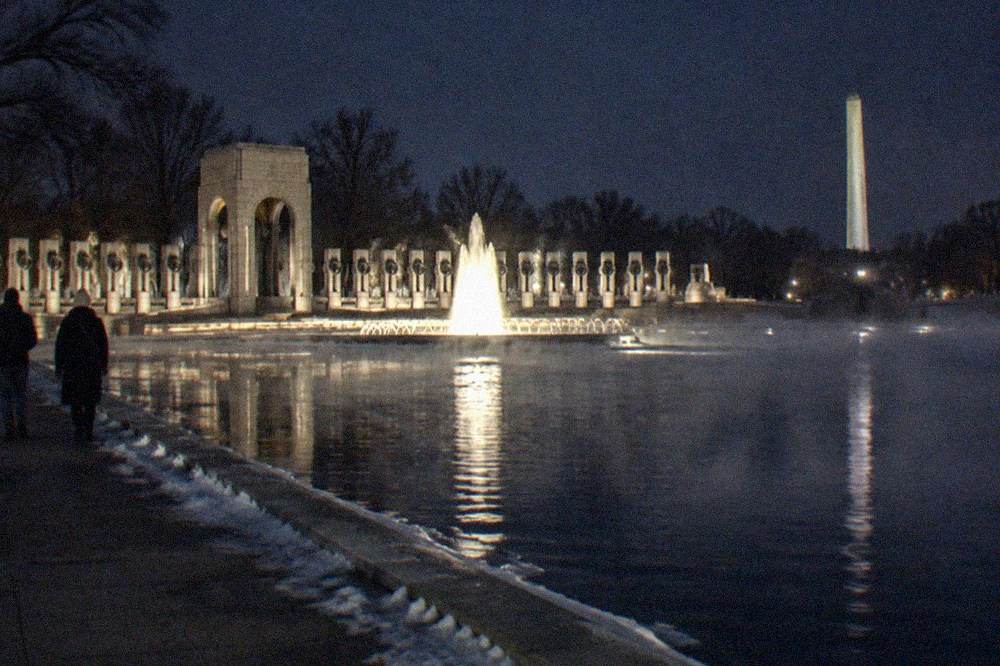 Illuminated World War II Memorial fountain and columns seen across the water at night