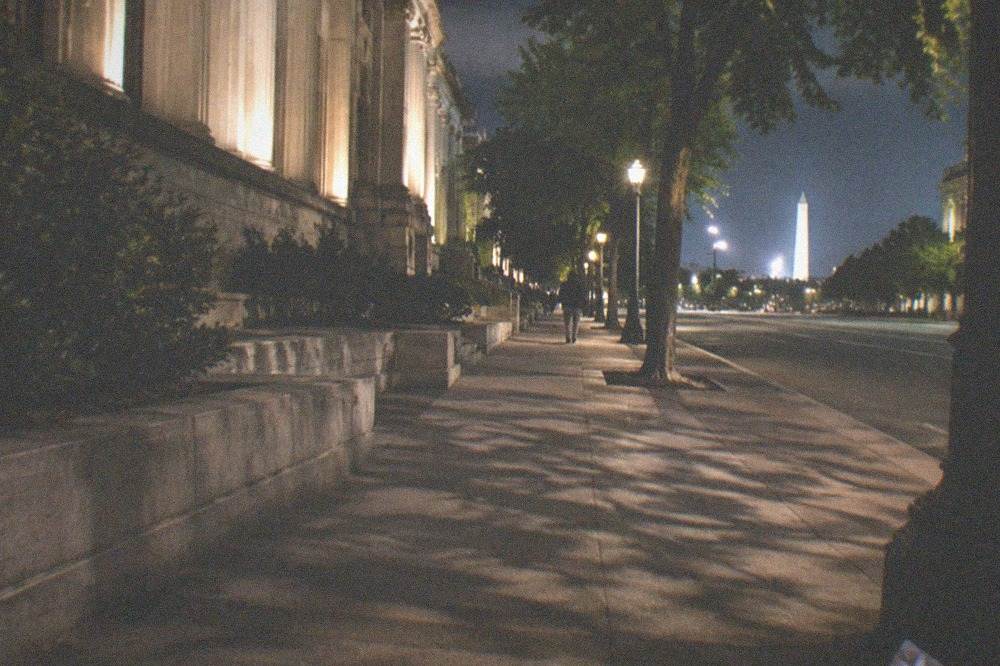 Empty lit walkway along the National Mall with monuments glowing in the distance at night