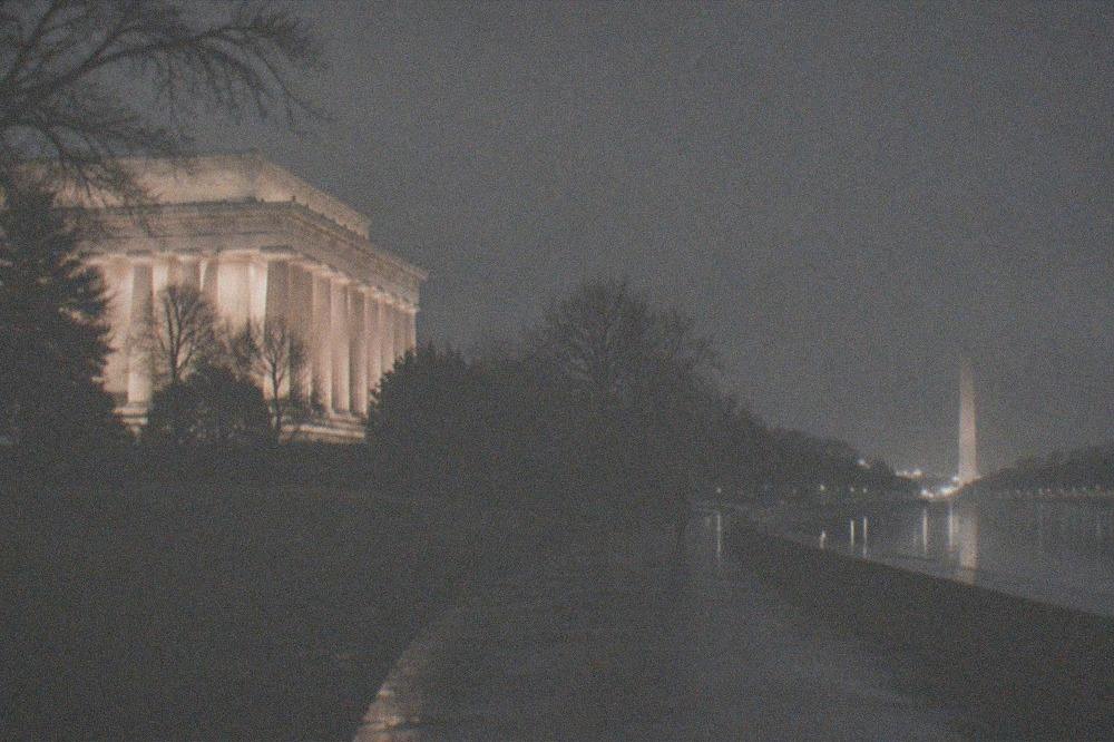 A quiet illuminated walkway near the National Mall at night with distant memorial lights and an empty path