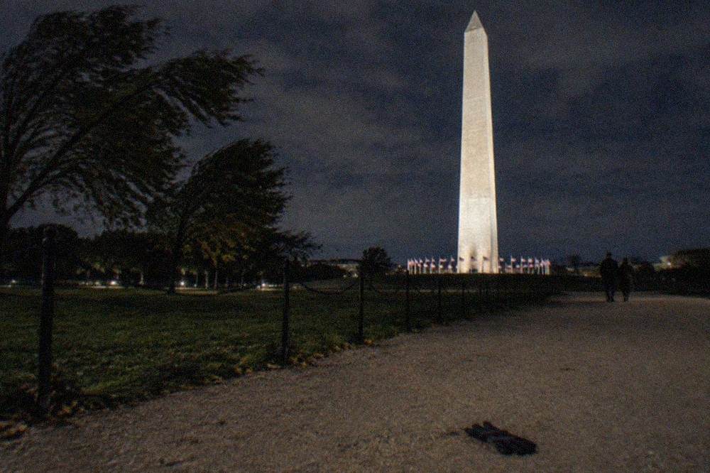 The illuminated Washington Monument obelisk rising above dark tree lines along the National Mall
