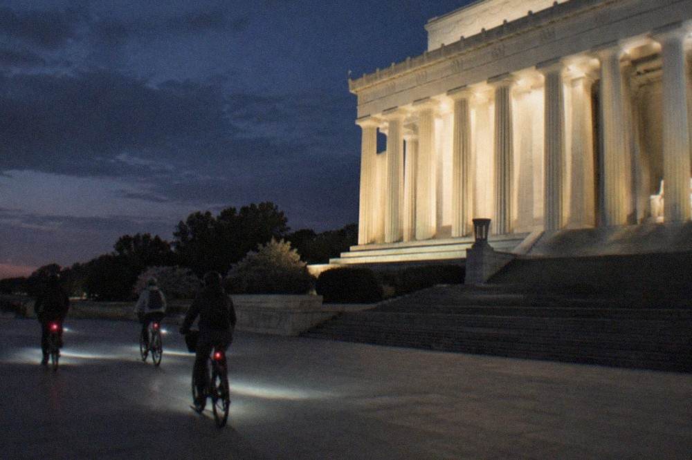 Small group of cyclists riding past illuminated memorial columns on the National Mall at night