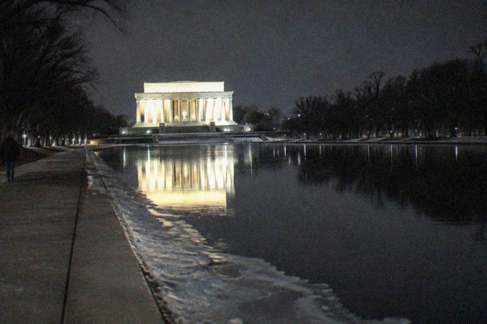 Illuminated Lincoln Memorial reflecting in water at night with empty surrounding walkways