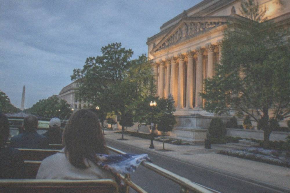 Tour trolley with passengers passing lit federal buildings on a Washington DC evening