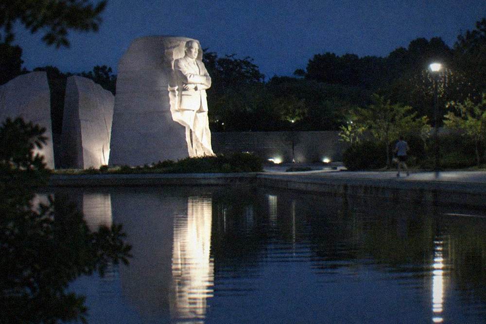 An illuminated memorial facade reflected in still water on the National Mall at night