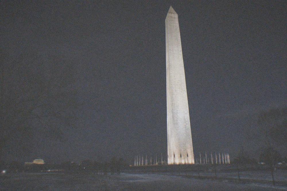A lit memorial arch and columns standing above dark parkland on the National Mall