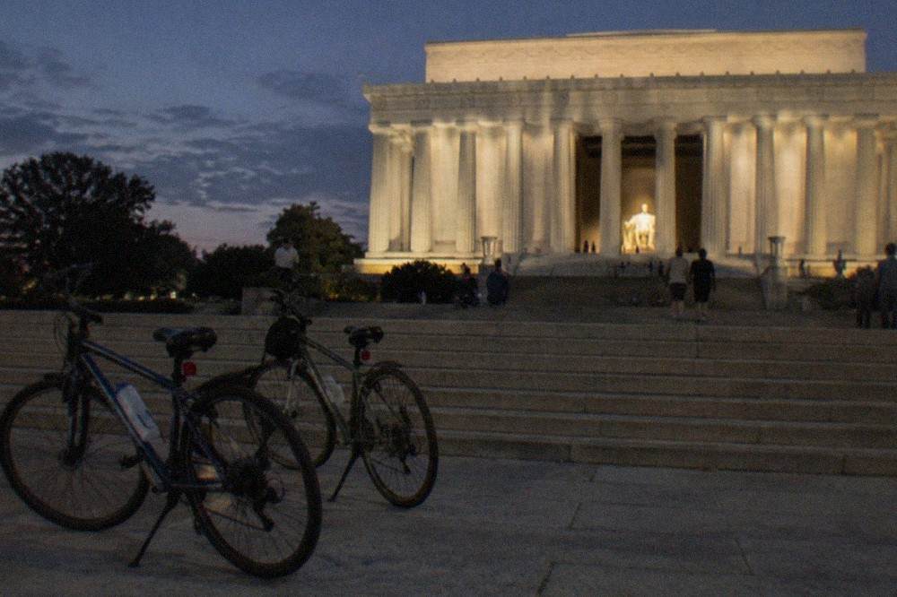 Riders on a guided night bike tour pause at the Lincoln Memorial, the statue glowing inside the colonnade.