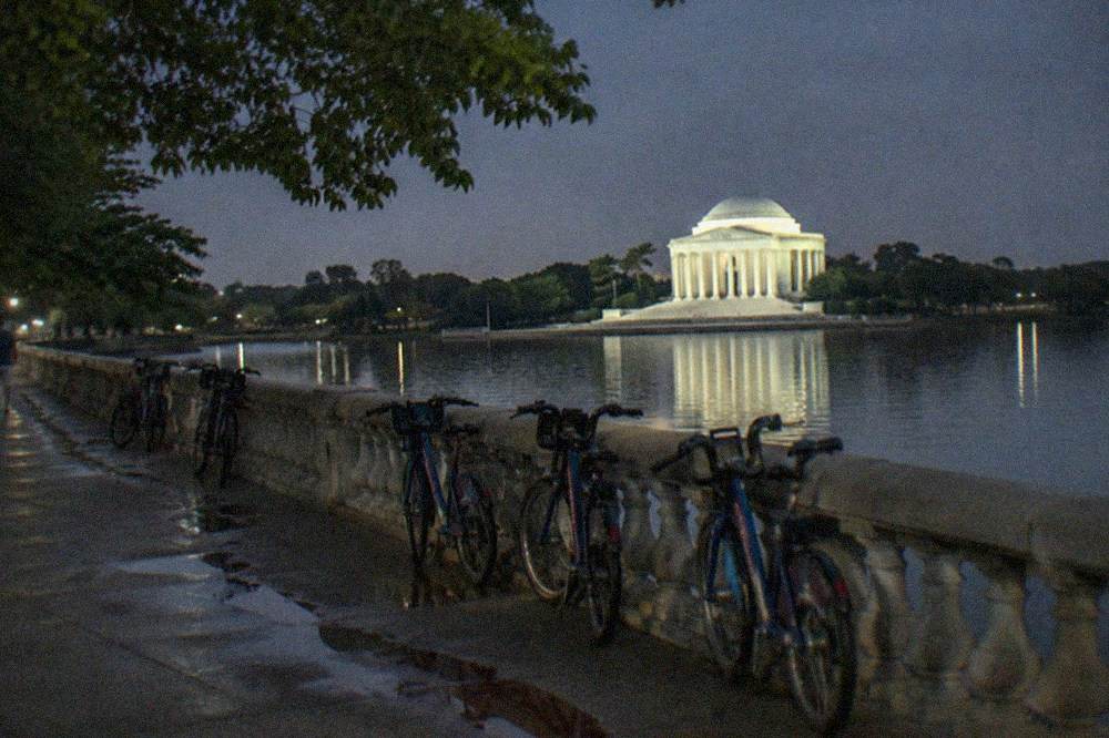 A group of cyclists on a guided night tour, bikes lined up near the Jefferson Memorial with the Tidal Basin in the background.