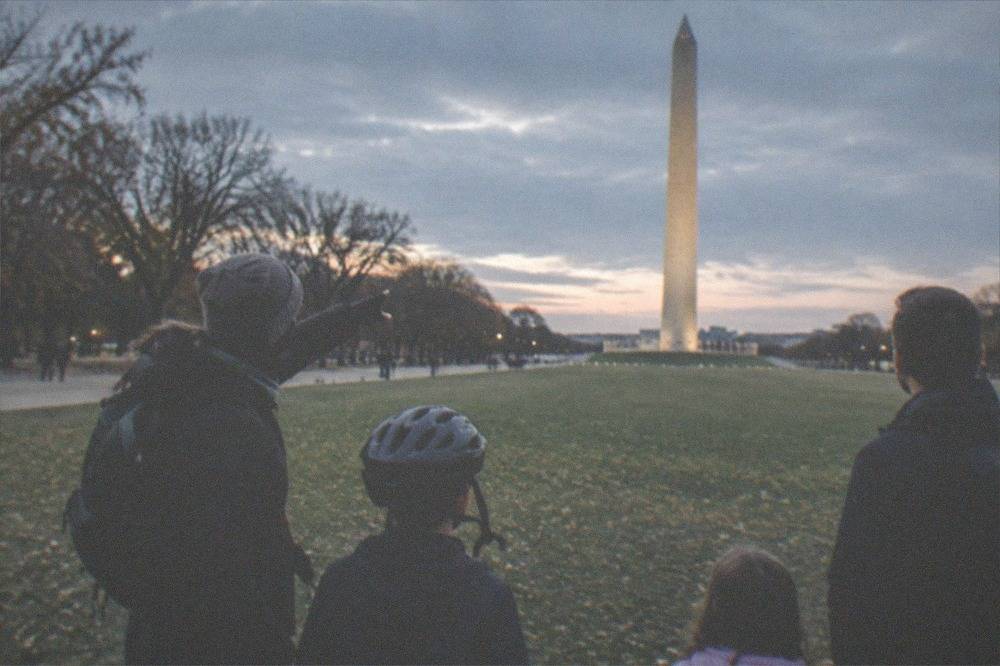 A small family on a private night bike tour, the guide pointing toward the Washington Monument lit against a dark sky.