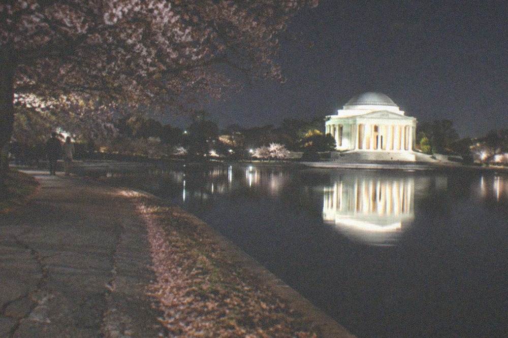 The illuminated Jefferson Memorial dome reflected in the Tidal Basin, with a bike path curving along the water's edge.