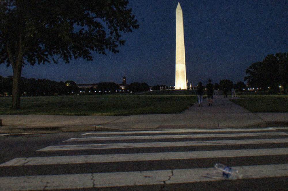 The Washington Monument lit against a dark sky above the National Mall lawns