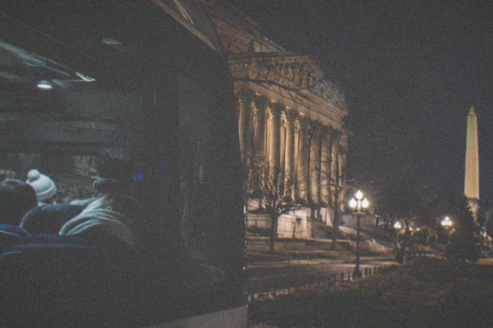 Tour passengers seated inside a lit vehicle at night with monuments visible outside