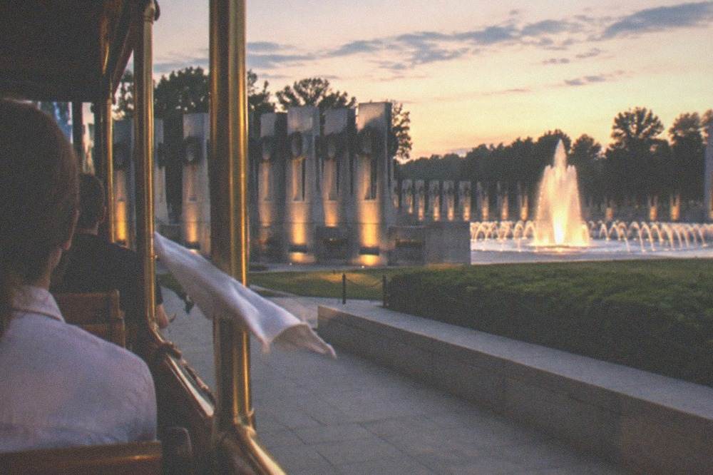 An open-air trolley passing the illuminated World War Two Memorial at night