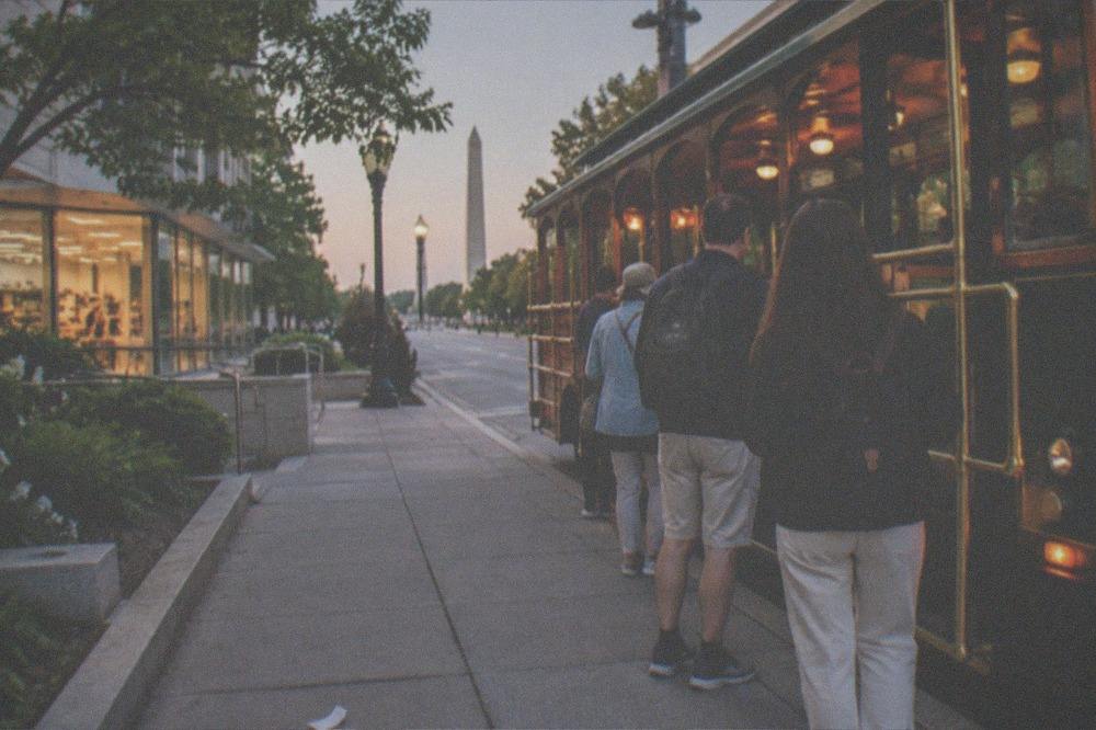A lit tour vehicle waiting at a curb near the National Mall at dusk